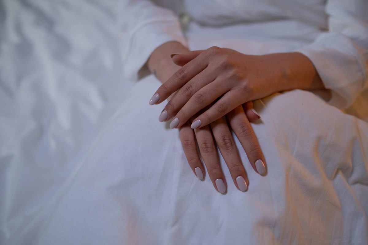 Mains aux ongles nude posées sur un drap blanc